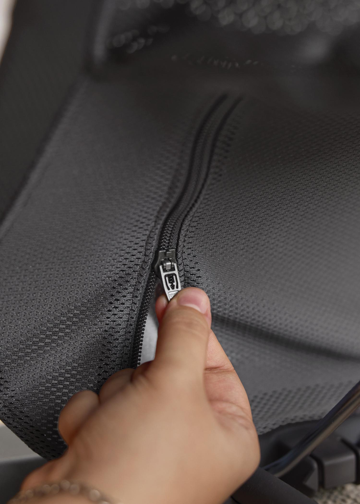 A close-up of a hand gripping a zipper on textured black fabric.